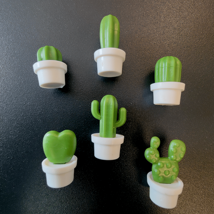een groep koelkastmagneten van kleine cactussen in witte potten