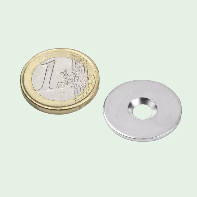 Metalen tegenstuk van 23mm met gat naast een euromunt om de grootte in te schatten