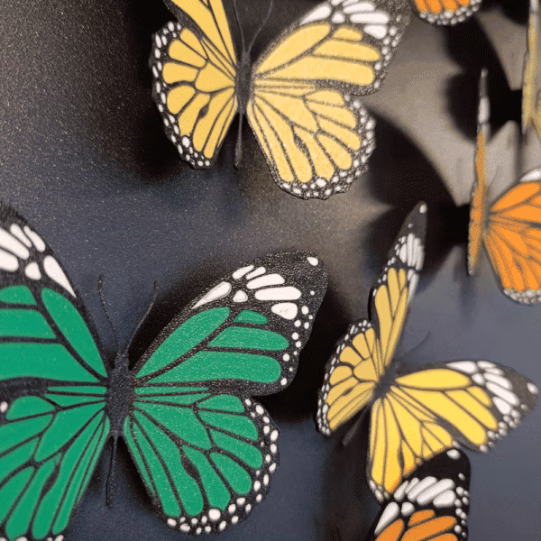 Met de 3D printer gemaakte koelkastmagneten in vlindervorm en in drie kleuren geel, groen en oranje op een zwart magneetbord