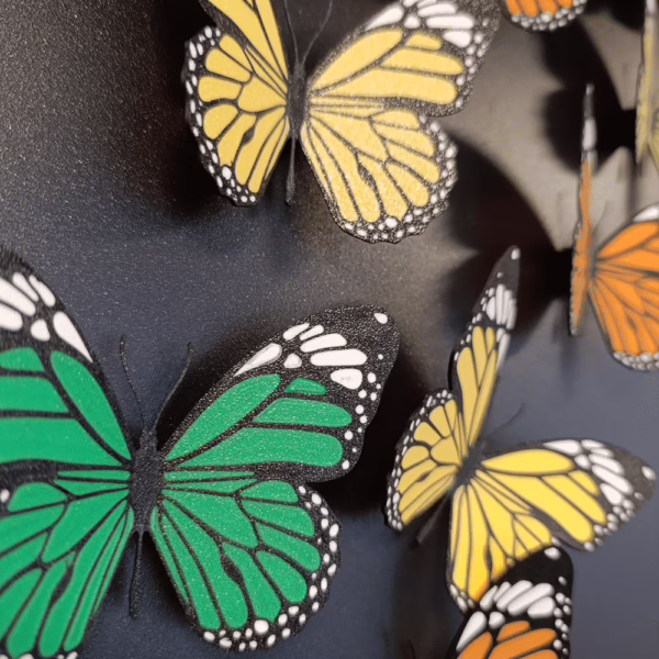 Met de 3D printer gemaakte koelkastmagneten in vlindervorm en in drie kleuren geel, groen en oranje op een zwart magneetbord