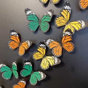 Met de 3D printer gemaakte koelkastmagneten in vlindervorm en in drie kleuren geel, groen en oranje op een zwart magneetbord